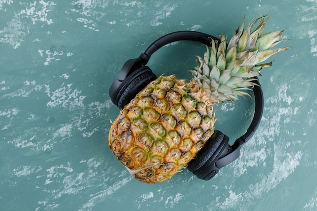 Pineapple with headphones on plaster surface