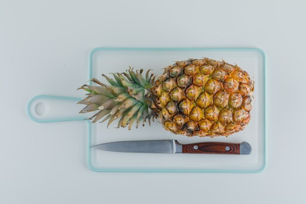 Pineapple with knife on white cutting board