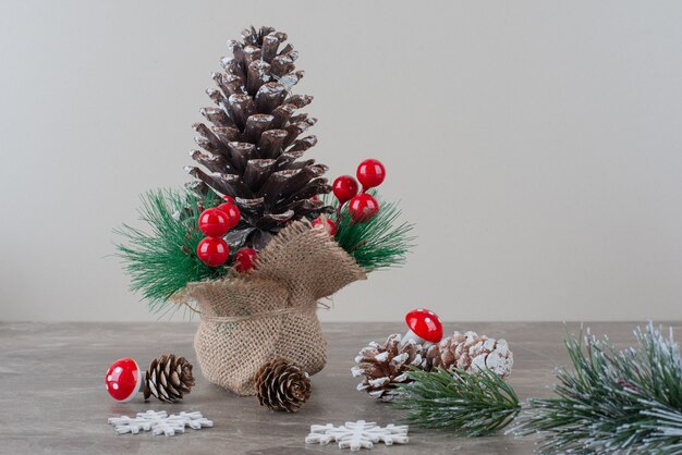 Pinecone decorated with holly berries and branches on marble table.