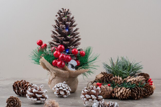 Pinecone decorated with holly berries and branches on marble table.