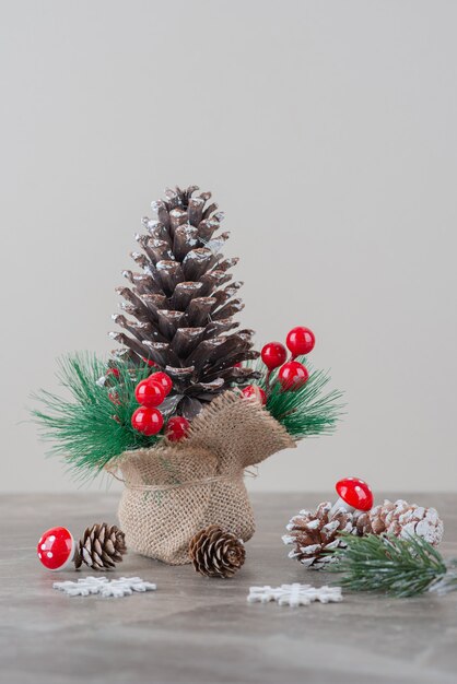 Pinecone decorated with holly berries and branches on marble table.