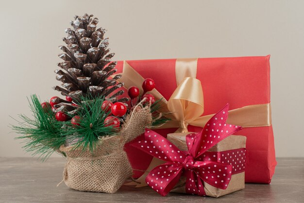 Pinecone decorated with holly berries and gift bags on marble table