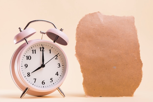 Pink alarm clock near the torn paper piece against beige background