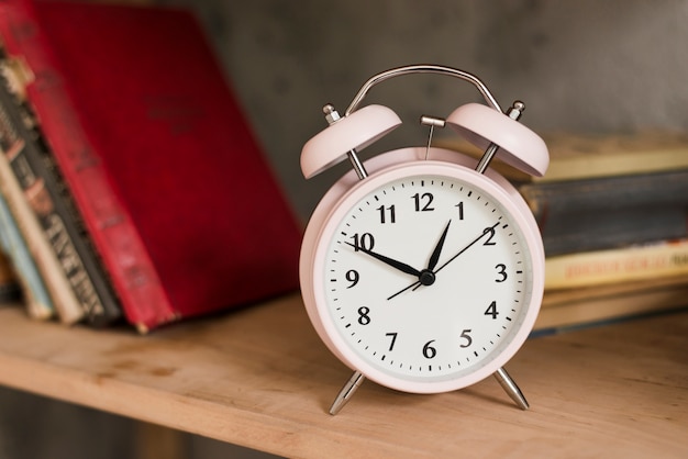 Pink alarm clock on wooden bookshelf