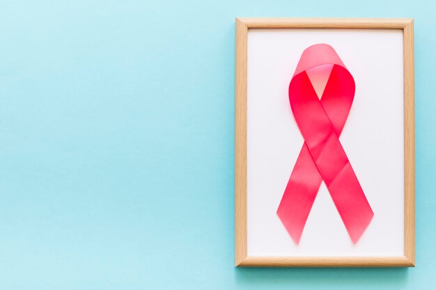 Pink awareness ribbon on white frame over the blue background