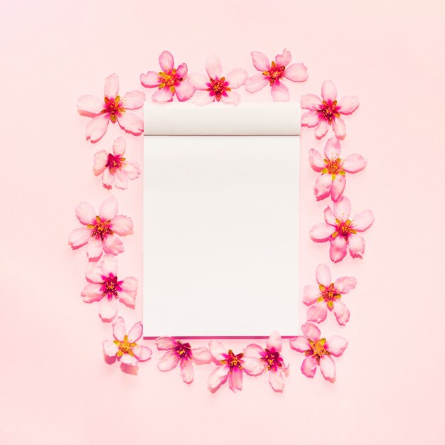 Pink background with notebook around flowers 