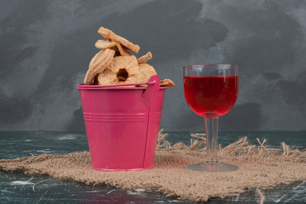 Розовая корзина с сухофруктами и стаканом сока на мраморной стене.