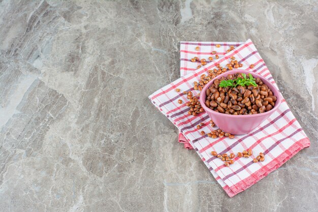 Pink bowl of boiled beans with tablecloth on marble surface.