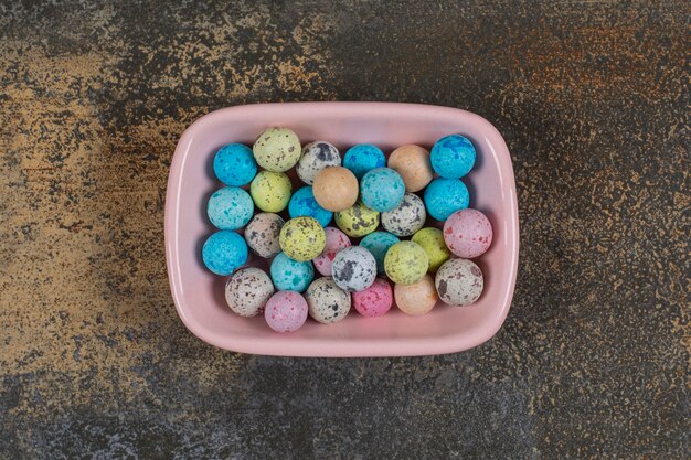 Pink bowl of colorful candies on marble.