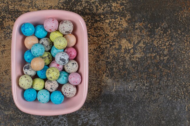 Pink bowl of colorful candies on marble.