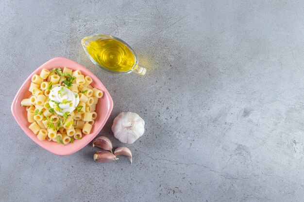 돌 배경에 올리브 오일과 함께 맛있는 삶은 파스타의 핑크 그릇.