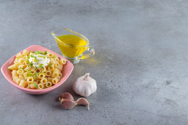 Pink bowl of delicious boiled pasta with olive oil on stone background. 