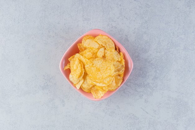 Pink bowl of delicious crunchy chips on stone background.