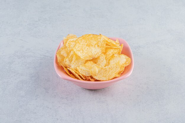 Pink bowl of delicious crunchy chips on stone background.