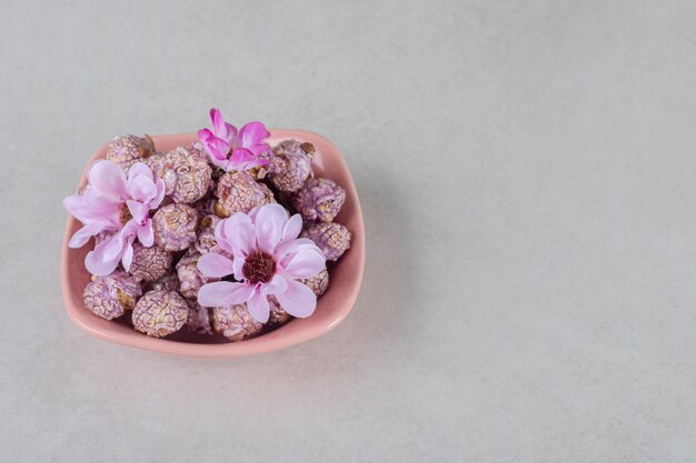 Pink bowl full of flavored popcorn decorated with flowers on marble table.