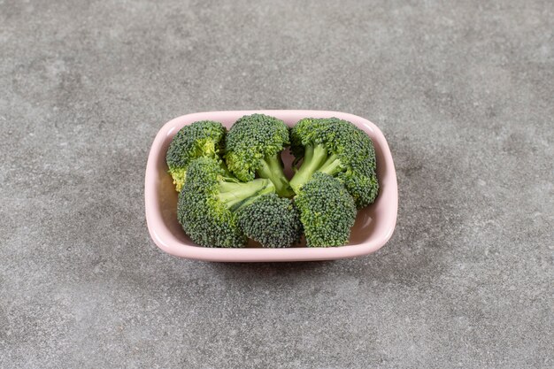 Pink bowl of healthy fresh broccoli on stone background.