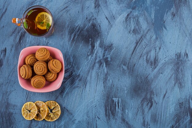 Pink bowl of mini cinnamon cakes with glass of tea on stone background. 