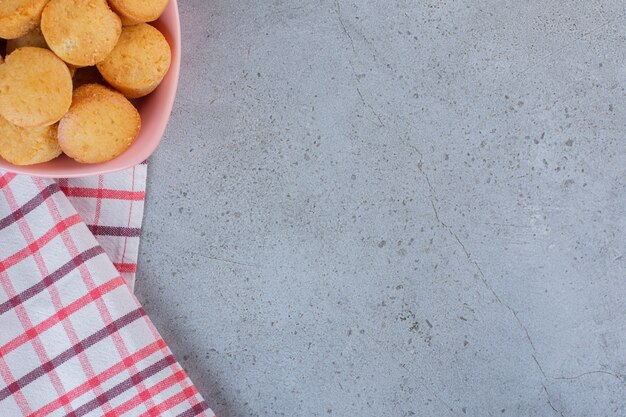 Pink bowl of mini sweet cakes on stone table.