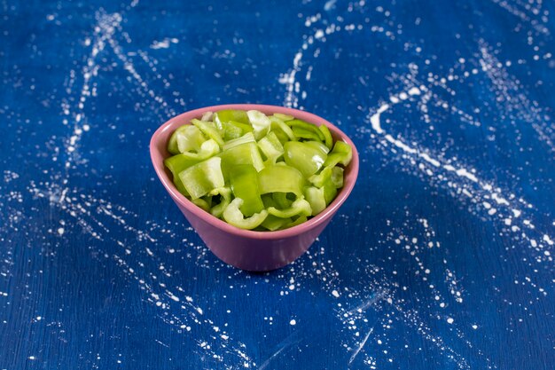 Pink bowl of ripe green bell peppers on marble table.