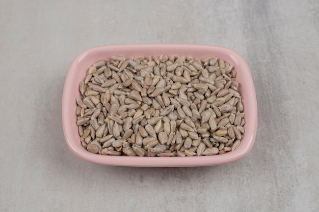 Free photo pink bowl of roasted sunflower seeds on marble background.