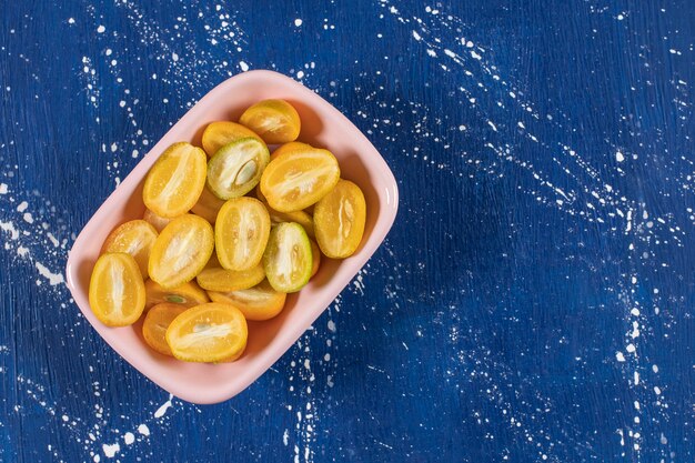 Pink bowl of sliced fresh kumquat fruits on marble surface