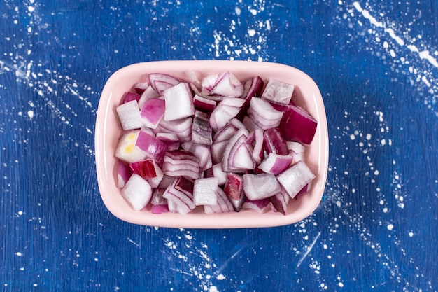 Pink bowl of sliced purple onions on marble surface