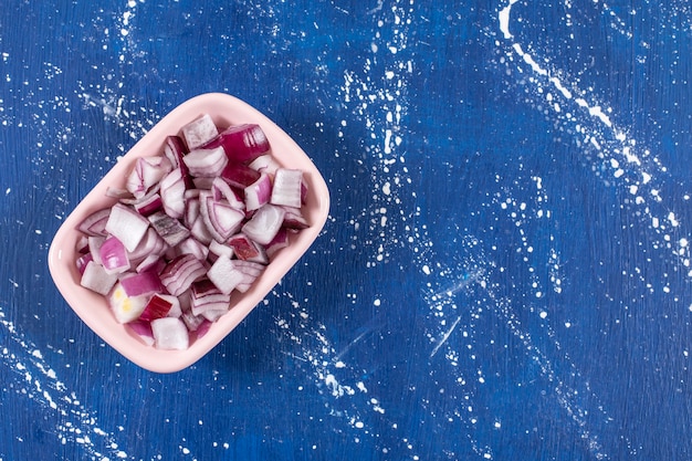 Pink bowl of sliced purple onions on marble table.