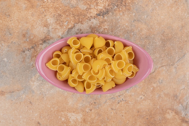 A pink bowl of unprepared macaroni on marble background. High quality photo