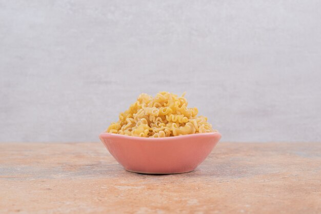 A pink bowl of unprepared macaroni on marble background. High quality photo
