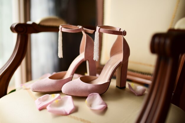 Розовая обувь невесты стоит на стуле с розовыми лепестками роз