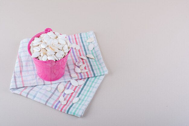 Pink bucket full of organic pumpkin seeds on white background. High quality photo