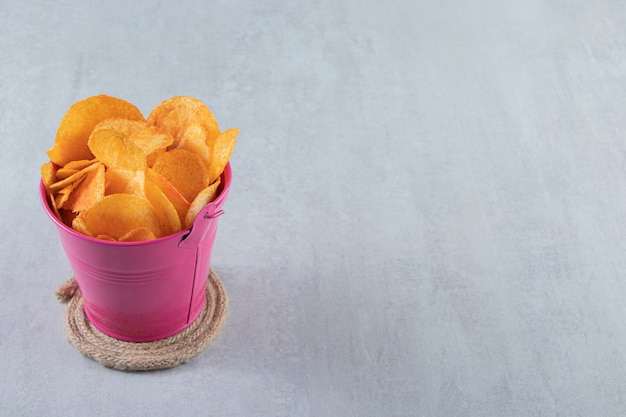 Pink bucket of spicy chips placed on stone.