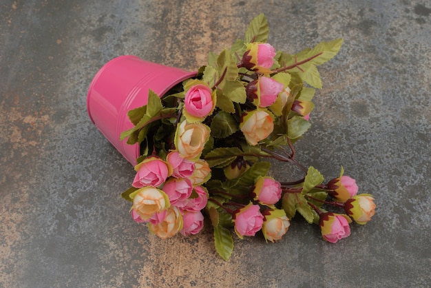A pink bucket with bouquet of flowers on marble surface.