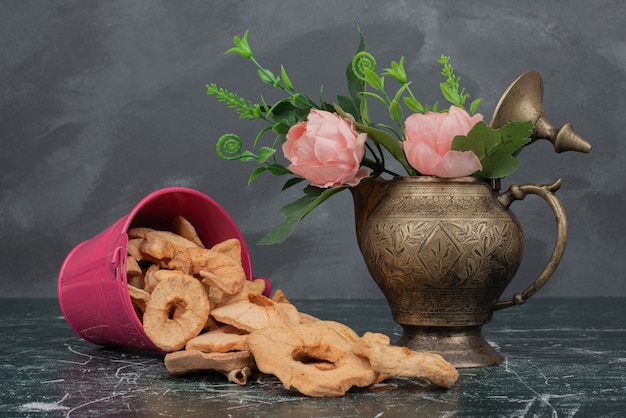 Розовое ведро с сушеным яблоком и ваза с цветами на мраморном столе