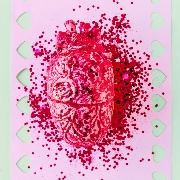 Free photo pink ceramic human heart with spangles on paper