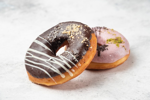 Pink and chocolate donuts with cream and walnut crumbs on white table. 