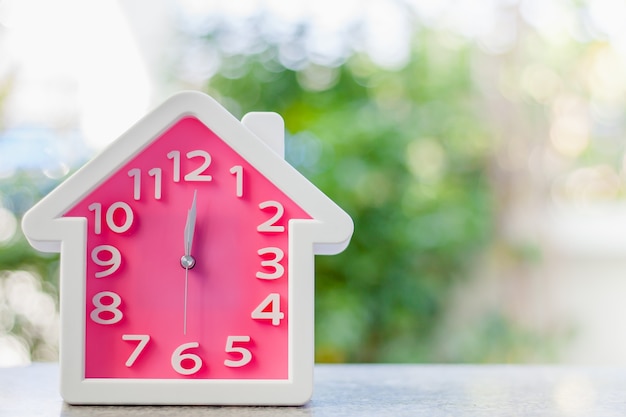 ぼんやりした​自然​の​緑​の​背景​に対して​12​時​の​家​の​形​の​ピンク​の​時計