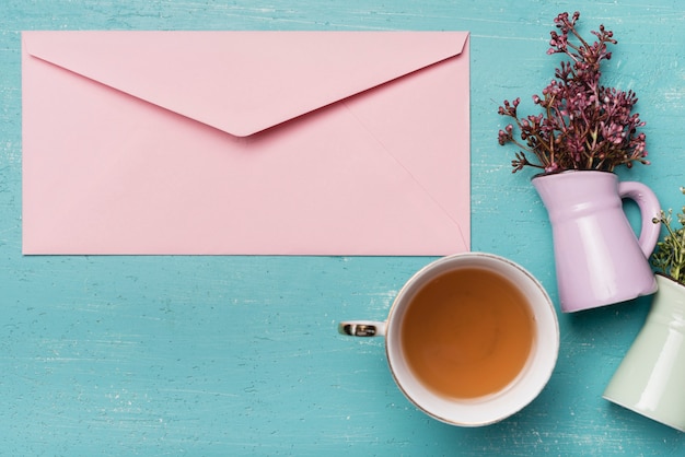 Pink closed envelope with vase and tea cup on blue wooden background