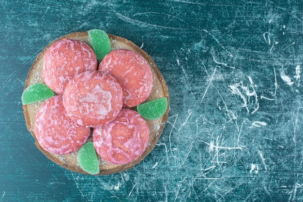 Pink coated cookies and marmelades on a wooden board on blue.