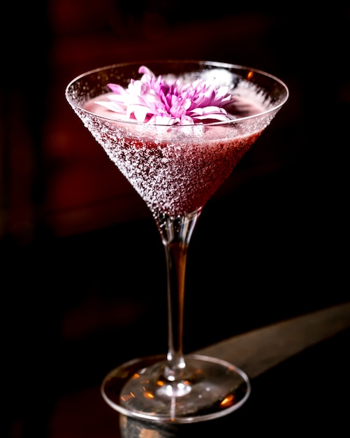 Pink cocktail garnished with flower in martini glass
