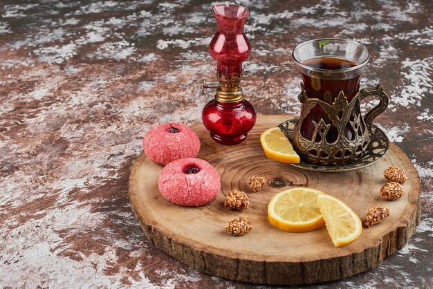 Розовое печенье и стакан чая на деревянной доске.
