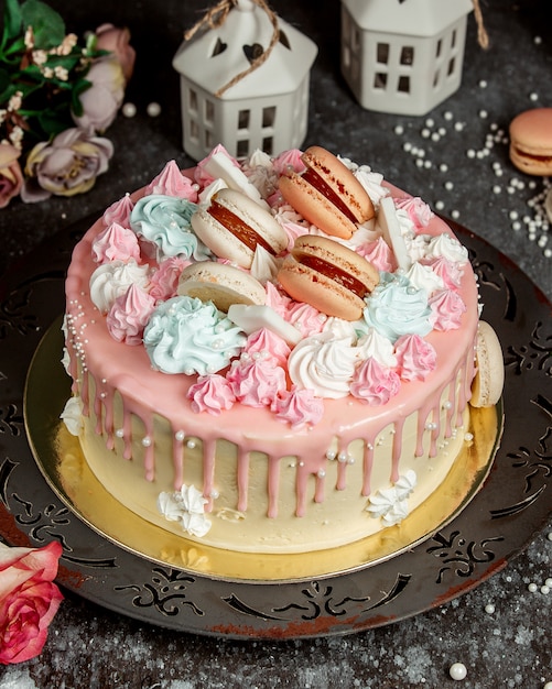 Pink cream drip cake garnished with pink and blue creams and macaroons