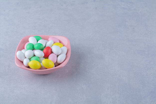 Розовая глубокая тарелка, полная красочных конфет на сером фоне. Фото высокого качества