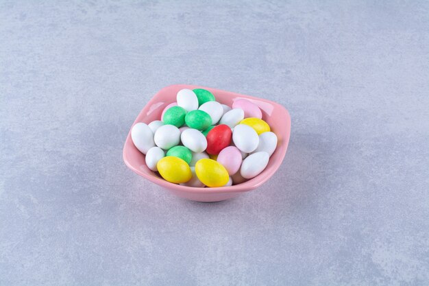 A pink deep plate full of colorful bean candies on gray table. 