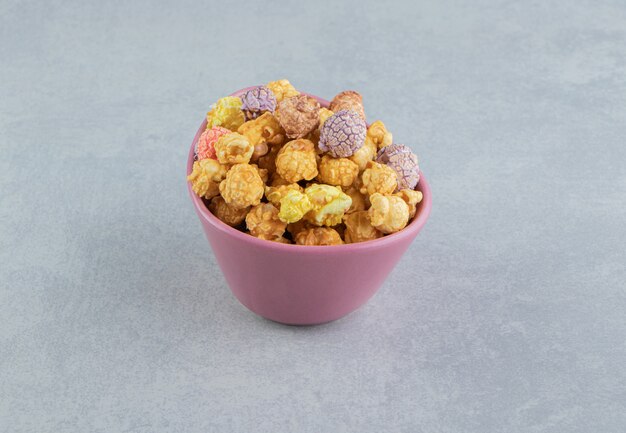 Розовая глубокая тарелка сладкого разноцветного попкорна.