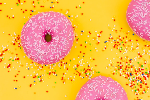 Pink donuts with colorful sprinkles on yellow background