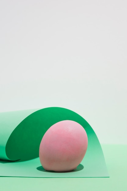Розовое пасхальное яйцо с листом бумаги на светлом столе