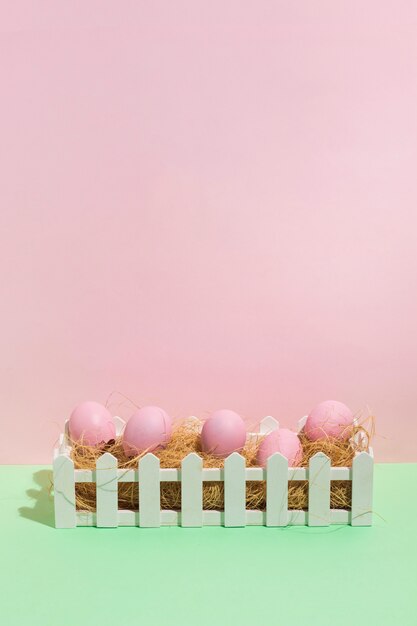 Розовые пасхальные яйца на сене в коробке на столе
