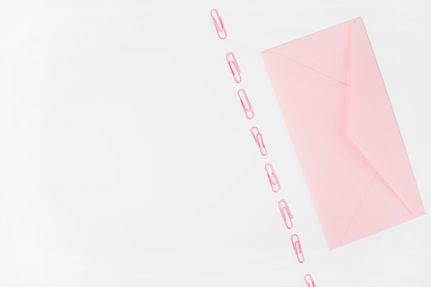 Pink envelope and paper clips on white background