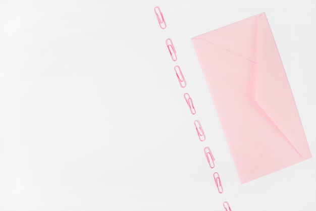 Розовый конверт и скрепки на белом фоне